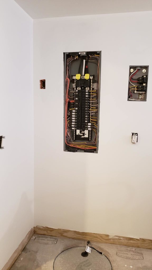 Electrical service panels and outlets without covers on a primed wall in a basement.